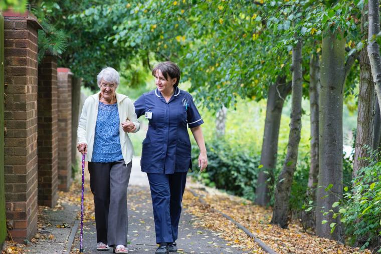 An elderly woman walking outside with her carer.