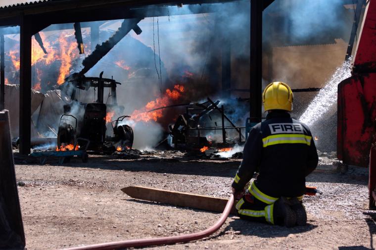 Firefighter knelt on ground fighting a fire in a barn.